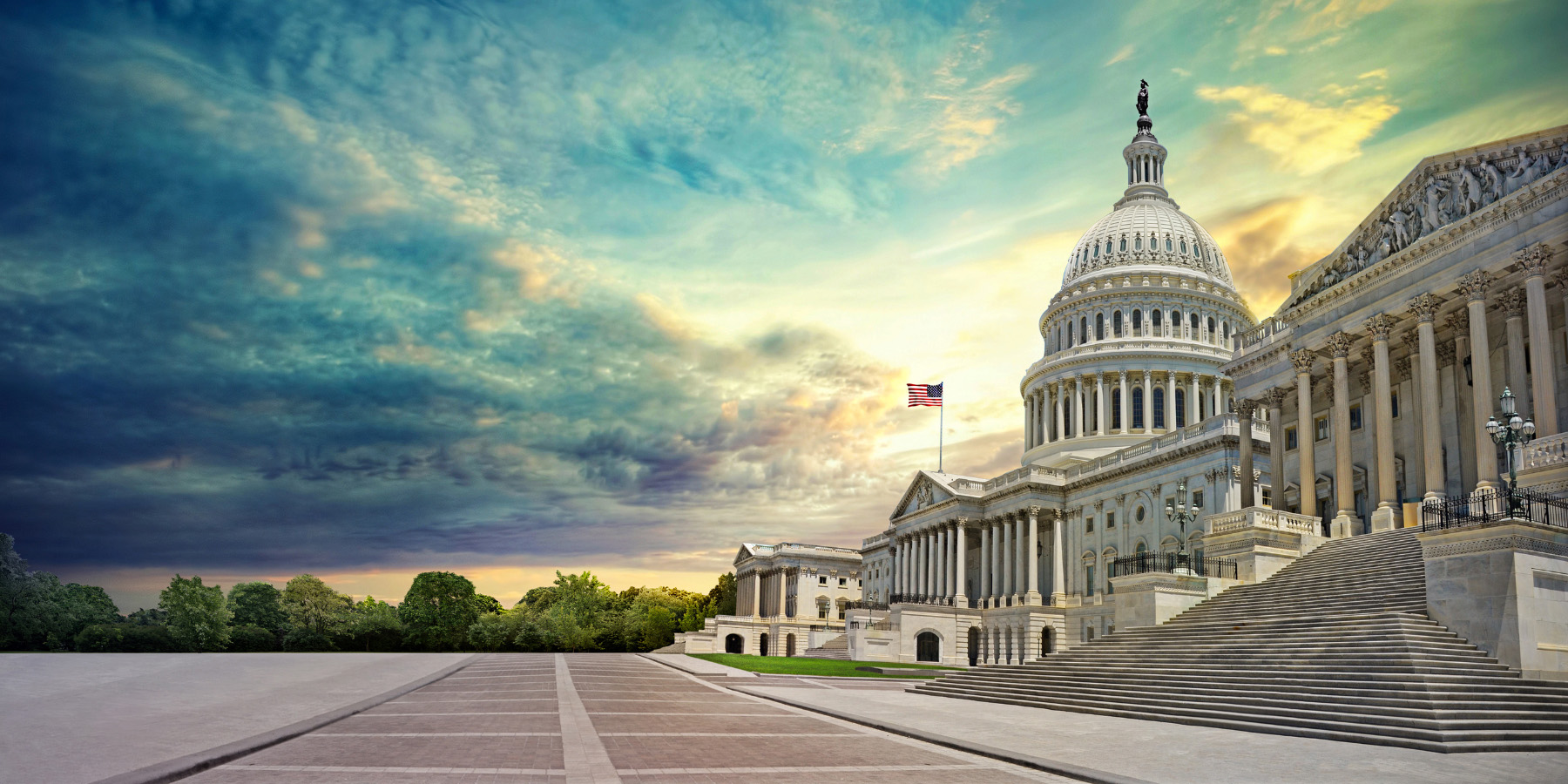 Capitol building at right, with walkway at center and cloud filled darker sky above