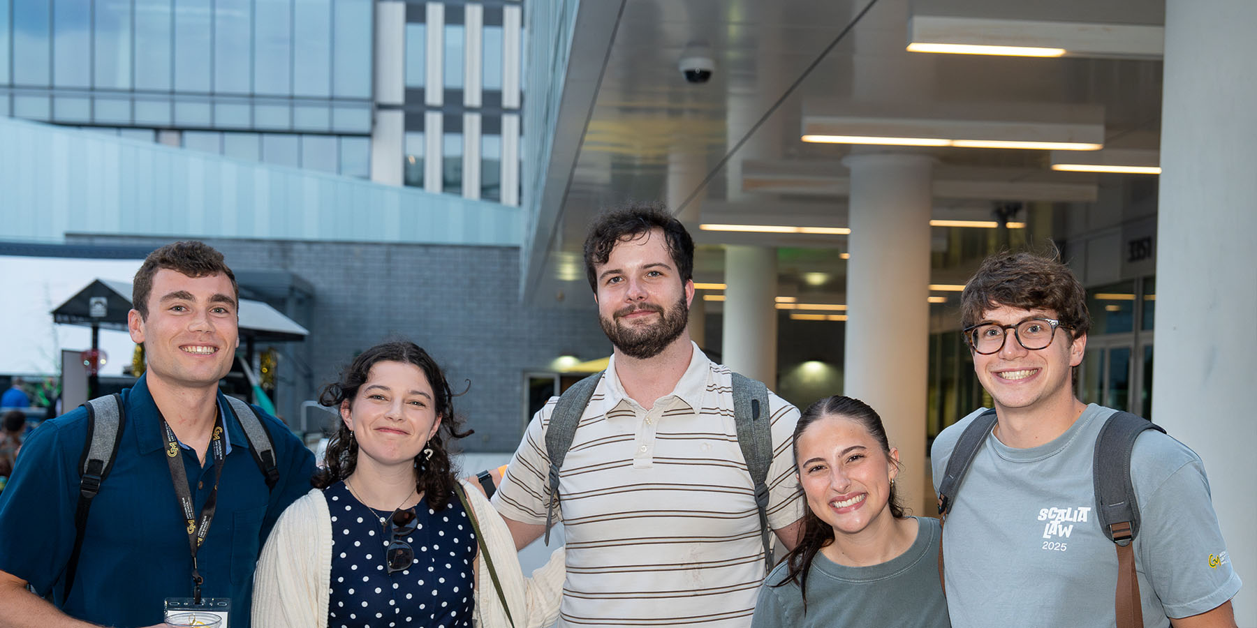Group of people in suits, men and women, smiling and facing camera.  Most are slightly blurry in background, one woman receives focus in foreground.