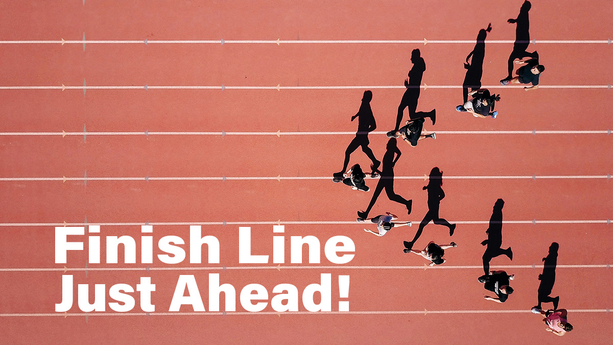 Runners in triangle formation on red track with white lines prepare to run, with words "Finish line just ahead!" in white font at bottom left of image