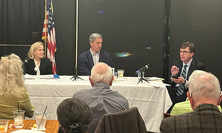 U.S. flag in background, table in front of it with panel members, and audience in foreground